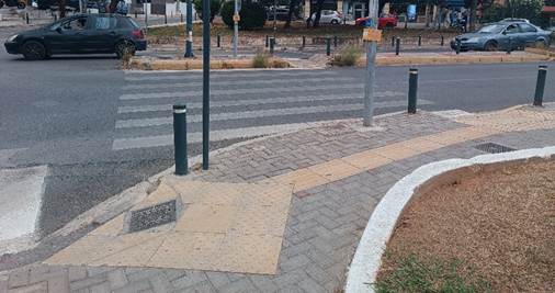 Διασταύρωση με φανάρια και δύο κίτρινες ράμπες που ενώνονται με κίτρινο οδηγό όδευσης τυφλών.