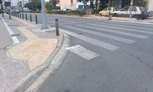 Διασταύρωση με φανάρια και μία κίτρινη ράμπα που διαθέτει κίτρινο οδηγό όδευσης τυφλών.