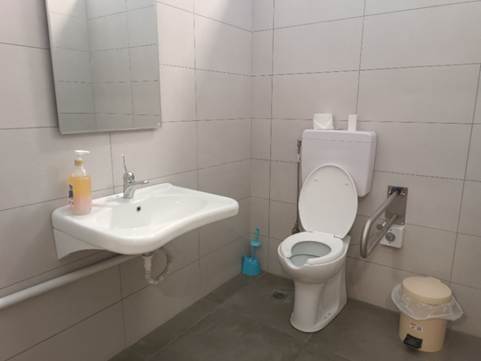 Εσωτερικός χώρος προσβάσιμου WC με νιπτήρα χωρίς εμπόδια στα αριστερά και λεκάνη με σπαστή μπάρα και καλαθάκι με ποδόπληκτρο στα δεξιά.